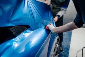 2 people installing a blue car wrap for a customer